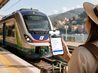 Viaggiatrice consulta sullo smartphone un’app di prenotazione treni davanti a un convoglio regionale in una stazione italiana