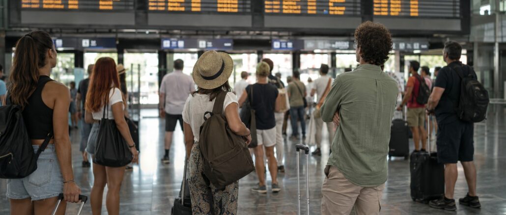 Viaggiatori in attesa davanti al tabellone partenze durante una giornata di scioperi nei trasporti.
