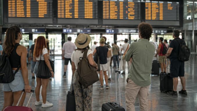 Viaggiatori in attesa davanti al tabellone partenze durante una giornata di scioperi nei trasporti.