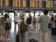 Viaggiatori in attesa davanti al tabellone partenze durante una giornata di scioperi nei trasporti.