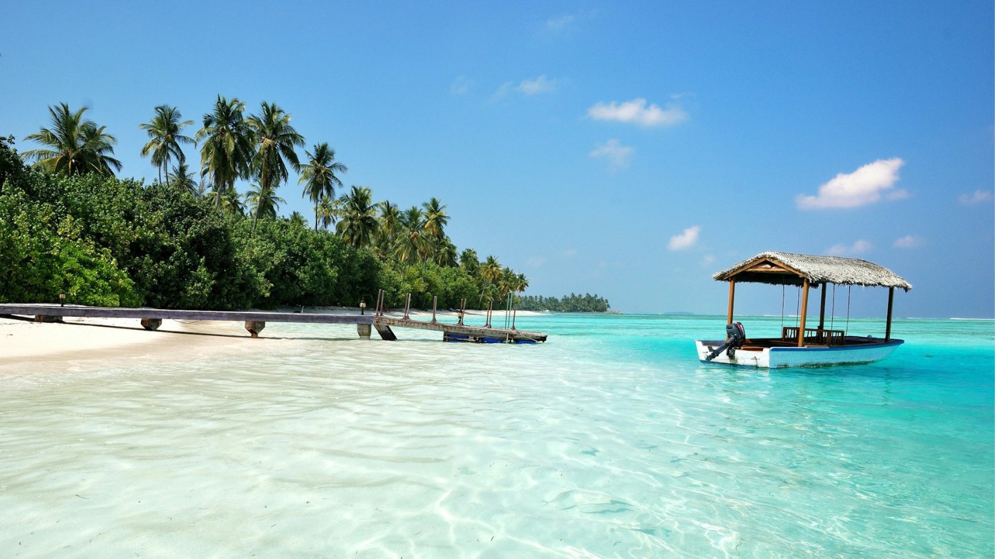Plage blanche des Maldives avec un bateau traditionnel sur le lagon turquoise.