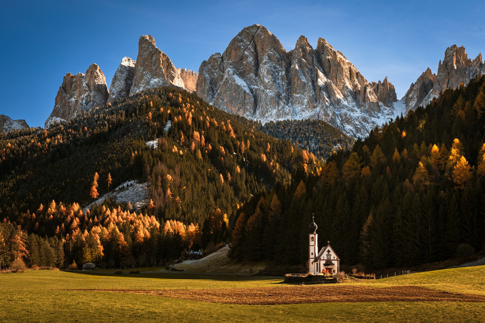 Chiesetta di San Giovanni in Ranui nella Val di Funes, con larici dorati e le cime delle Odle sullo sfondo