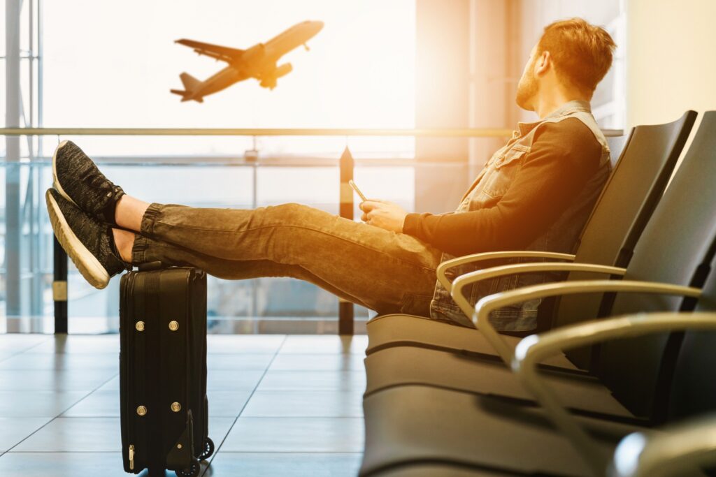 Viaggiatore in aeroporto in attesa della partenza con valigia e aereo sullo sfondo