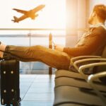 Viaggiatore in aeroporto in attesa della partenza con valigia e aereo sullo sfondo